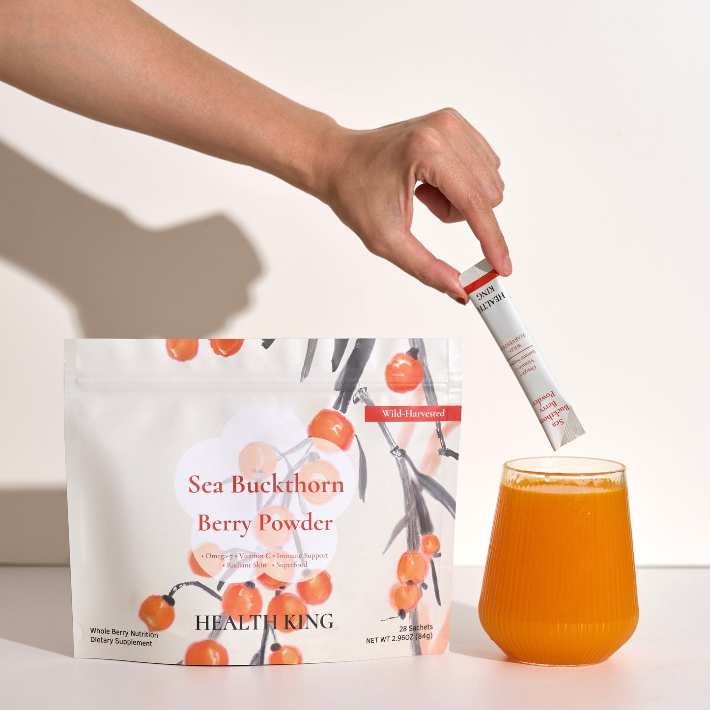 Person adding berry powder to a glass of juice with a package of Sea Buckthorn Berry Powder in the background.