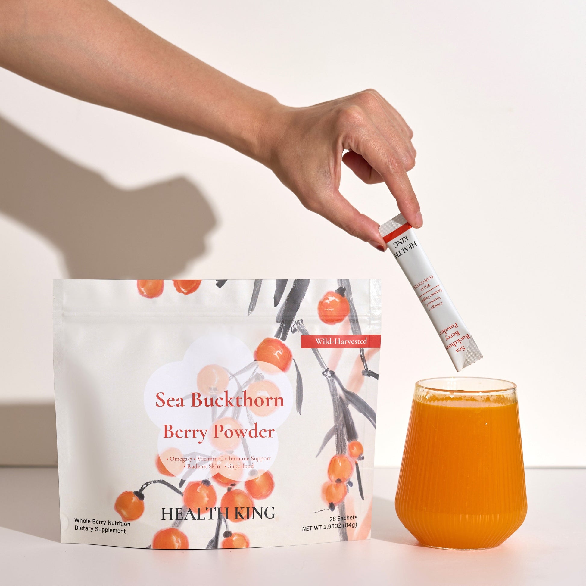 Person adding berry powder to a glass of juice with a package of Sea Buckthorn Berry Powder in the background.