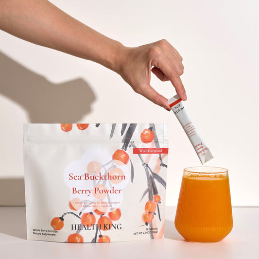 Person adding berry powder to a glass of juice with a package of Sea Buckthorn Berry Powder in the background.